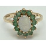 A 9ct gold ring set with central oval opal surrounded by a row of 12 emeralds. Fully hallmarked