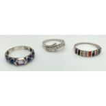 3 large size stone set silver dress rings. A crossover band style set with clear stones, a half