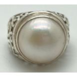 A silver and Mabe pearl dress ring with high set shoulders with pierced scroll detail. Marked 925 to