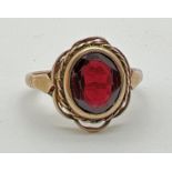 A vintage 9ct gold dress ring set with a central oval cut garnet. Scalloped and rope detail to