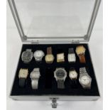 A metal and perspex watch display case containing 11 men's and women's modern wristwatches. To