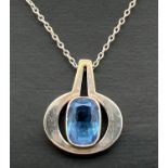A contemporary style silver pendant with bark decoration to sides and set with an emerald cut blue