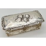 An Edwardian silver topped cut glass trinket box, lid embossed with cherub detail. Hallmarked to rim