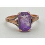 A 9ct gold dress ring set with a emerald cut amethyst stone. Simple decoration to shoulders.