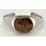A modern design cuff bangle set with a large piece of green Baltic amber. Hallmarks to back of
