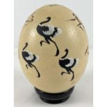 A hand painted ostrich egg decorated with an African hunting scene, on an ebony stand. Total