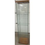 A modern square shaped glass cabinet with front opening full sized door and 3 interior glass