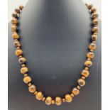 A 19" alternating larger and smaller Tigers Eye beaded necklace. Silver tone T bar clasp with floral