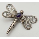 A vintage silver filigree brooch in the shape of a dragonfly, with central oval amethyst cabochon.