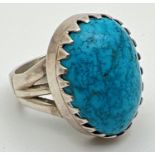 A silver statement dress ring set with a large turquoise cabochon and pierced detail to shoulders.