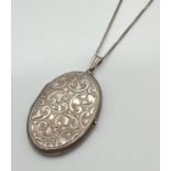 A vintage silver oval shaped locket with floral decoration to front and back. On a 24 inch fine curb