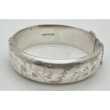 A 2 cm wide vintage silver hinged bangle with full floral decoration and safety chain. Hallmarked