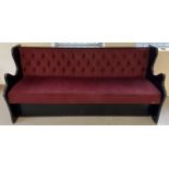 A vintage painted black wooden bench seat with button backed red velour upholstery and shaped
