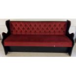 A vintage wooden bench seat painted black with button backed red velour upholstery and shaped
