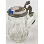 A vintage cut glass tankard with a hinged pewter lid holding a ceramic plaque. Aged repair to join
