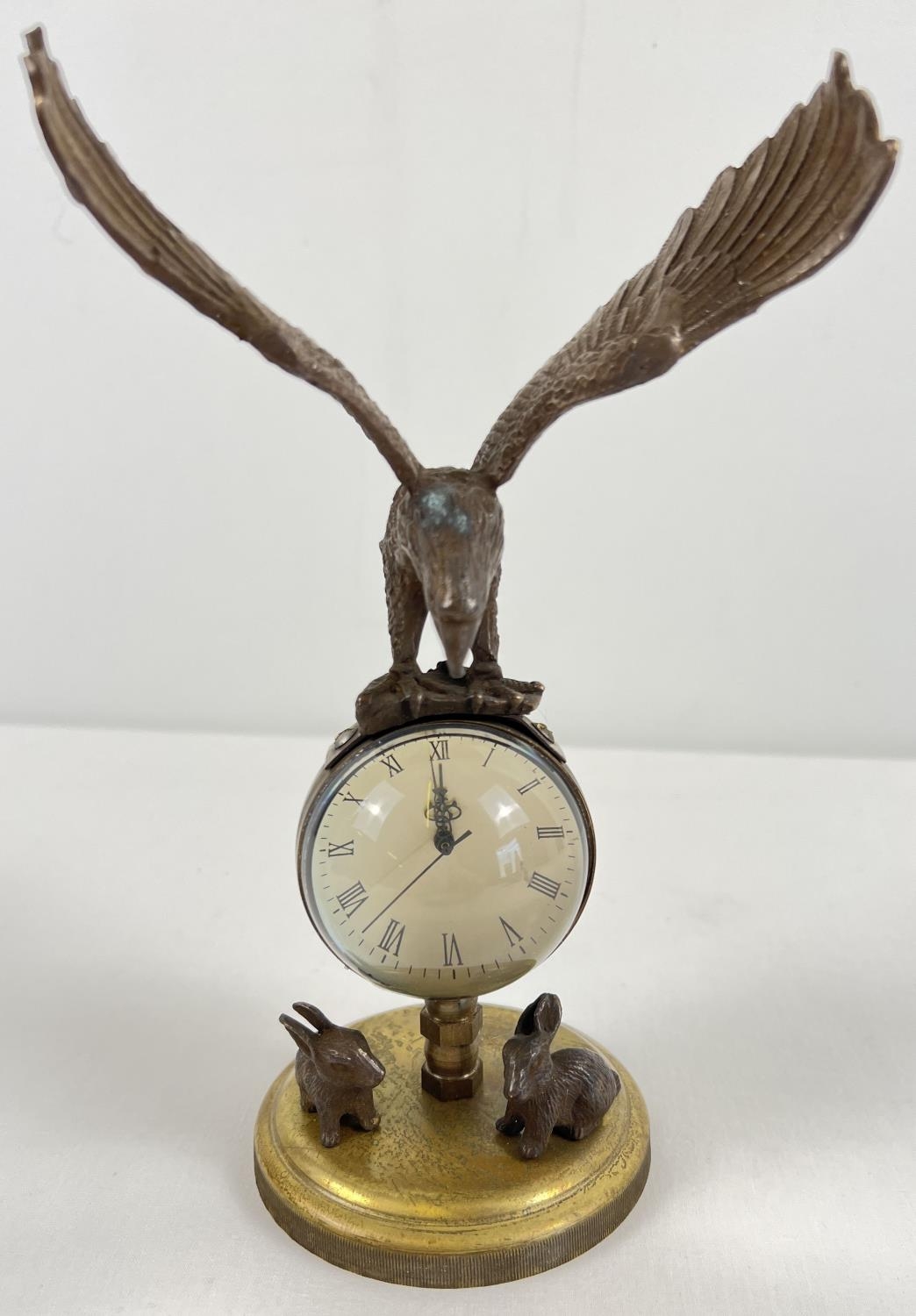 An ornamental brass ball clock with eagle shaped finial and rabbit figures to base. With wind up
