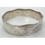 A heavy silver bangle with wave shaped edge. Full hallmarks to inside of bangle. Band width
