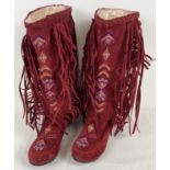 A pair of red faux suede moccasin boots with embroidered decoration and fringing to tops and side.