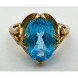 A 9ct gold dress ring set with a large oval cut Swiss blue topaz in a decorative mount. Full