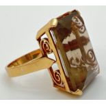 An 18K gold cocktail ring set with a large emerald cut smoked quartz stone. In claw set mount with