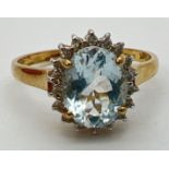 A 9ct gold aquamarine and diamond halo style dress ring. A central oval cut aquamarine (10mm x