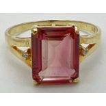 A 14K gold ring set with an emerald cut blush tourmaline and two small round cut diamonds to each