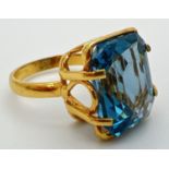 An 18k gold cocktail ring set with a large emerald cut Swiss blue topaz stone. Claw setting with