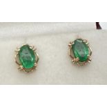 A pair of 9ct gold emerald set stud earrings with fluted edge mount. Each set with an oval cut