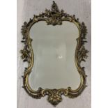 A antique gold coloured metal framed Rococo style shaped wall hanging mirror. With floral and scroll