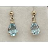 A pair of drop style gold earrings each set with a teardrop cut blue topaz stone. Complete with