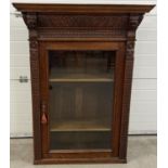 An antique dark wood wall hanging display cupboard with highly carved detail. With lion head