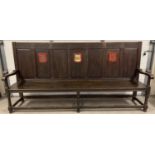 An antique dark wood high back settle bench with painted crest detail. Panelled back with carved