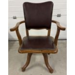 A vintage dark oak captains chair with 4 legged swivel base. Brown faux leather upholstery with
