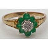 An unmarked 9ct gold, emerald and diamond ring in a flower shaped setting with decorative shoulders.