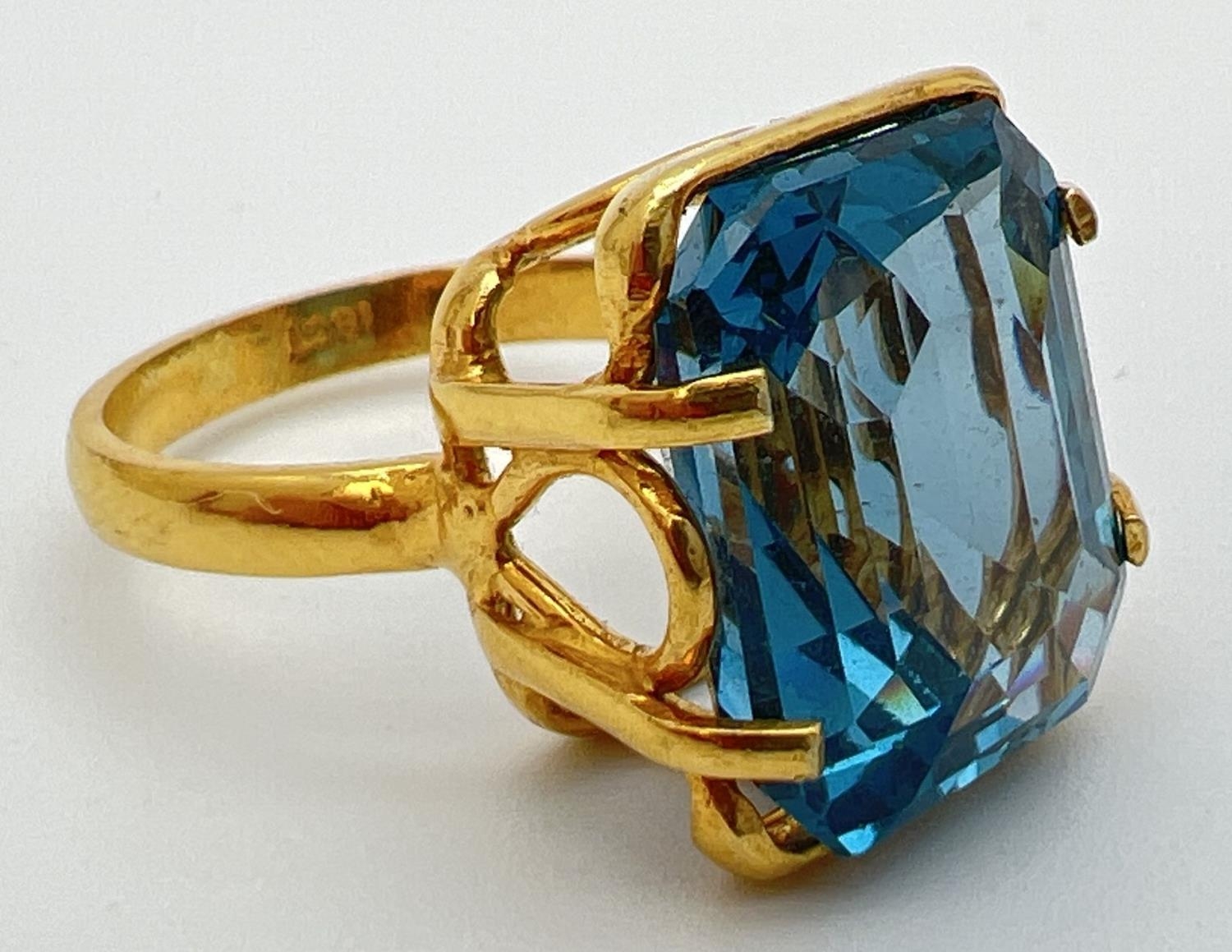 An 18k gold cocktail ring set with a large emerald cut Swiss blue topaz stone. Claw setting with