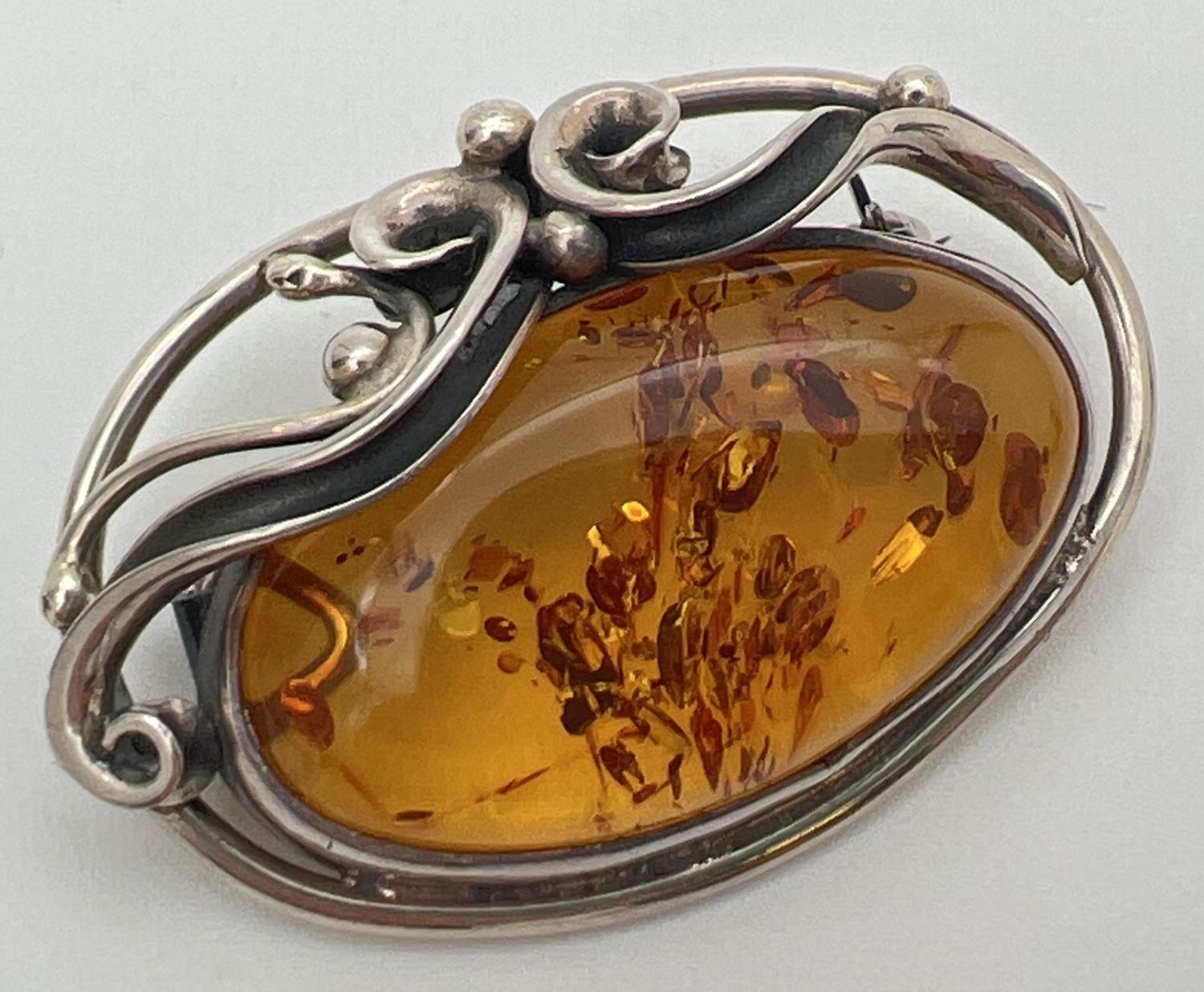 A silver and cognac Baltic amber brooch pendant of Art Nouveau design. With decorative swirl