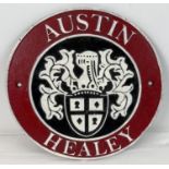 An Austin Healey circular shaped painted cast iron wall plaque. In red, black and white and with