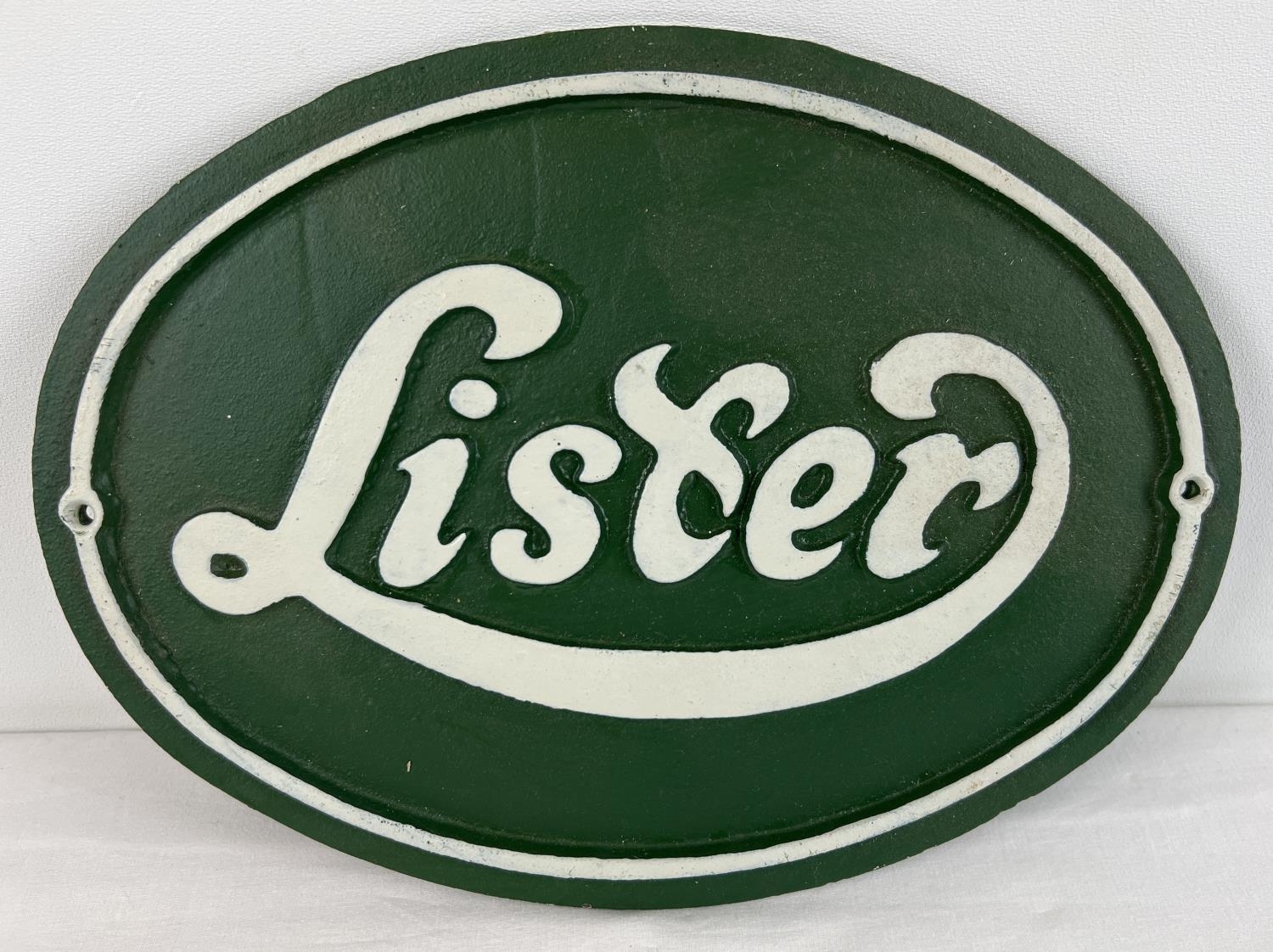 A green & white painted oval shaped cast iron wall plaque for Lister engines. With fixing holes.