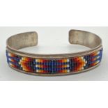 A Native American silver bangle with multi coloured small glass bead work panel set to front. Makers