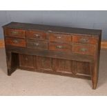 Low oak chest of eight small drawers, raised on shaped tapering end supports and with panelled back,