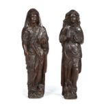 Two 17th Century carved oak standing figures, the first clutching a book in one hand, the other hand