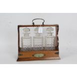 Edwardian oak tantalus, the silver plate mounted oak body containing three square decanters, with