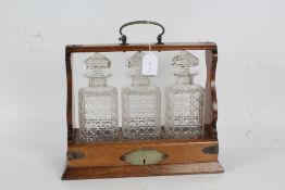 Edwardian oak tantalus, the silver plate mounted oak body containing three square decanters, with