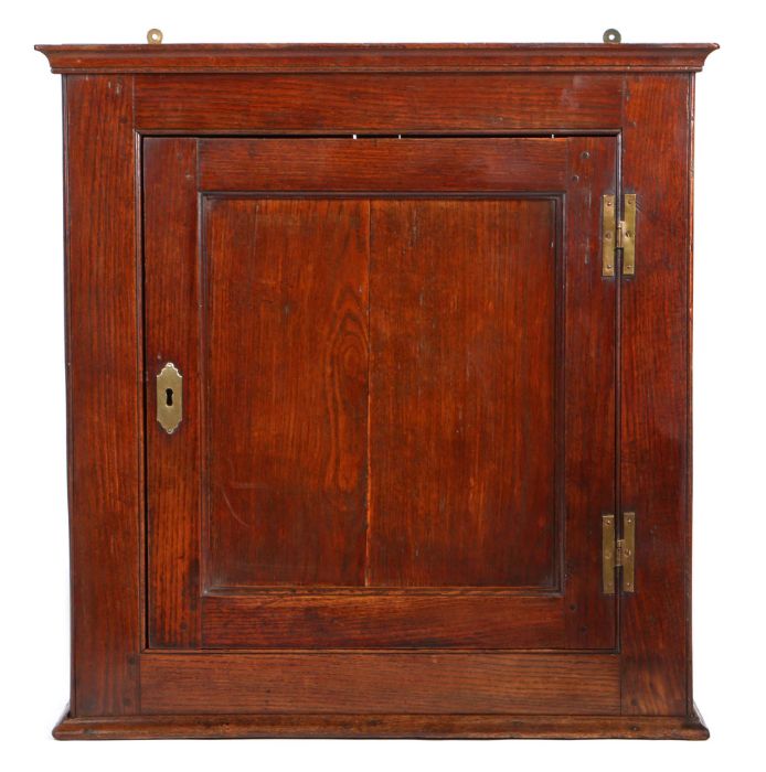 A George II joined oak wall cupboard, circa 1750, having a single-panelled cupboard door, framed by