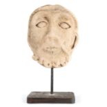 A Romanesque carved stone head, probably 12th century, French, with linear incised hair, curled