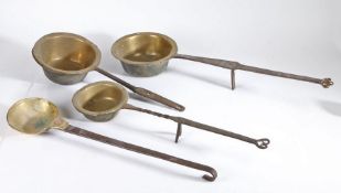 A collection of four early 18th Century brass and steel cooking pots, each with a brass pan and