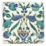 A 17th century Iznik tile, designed with a flower -filled vase, in blues, blacks and turquoise,