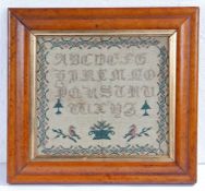 A William IV needlework sampler, circa 1830, with alphabet above an urn of flowers and two birds on