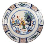 An 18th century Delft polychrome dish, the central oriental figures by a fence within a garden, the