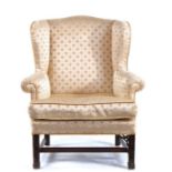 A George III mahogany and upholstered wingback armchair, the serpentine headed padded back, squab-